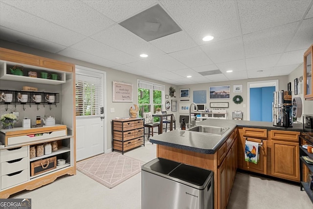 kitchen with sink, kitchen peninsula, a drop ceiling, and light colored carpet