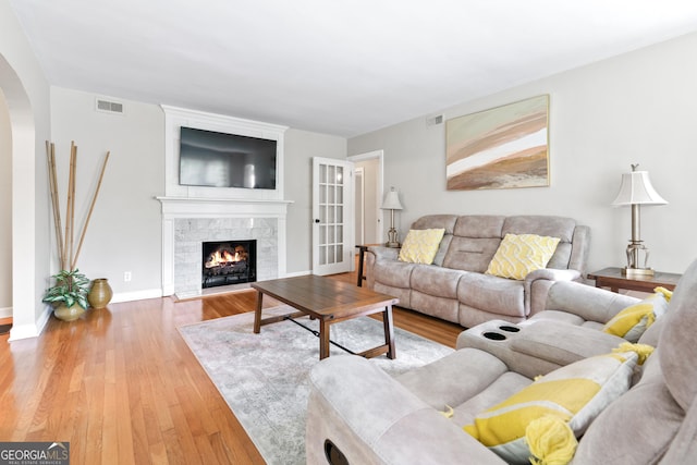 living room with visible vents, arched walkways, wood finished floors, and a tiled fireplace