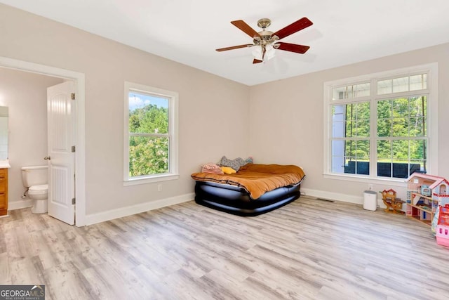 bedroom with light wood-type flooring, ceiling fan, and connected bathroom