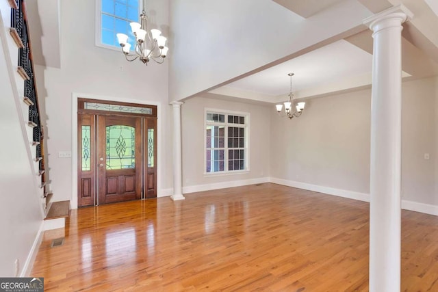 foyer entrance with wood-type flooring, ornate columns, a chandelier, and a high ceiling