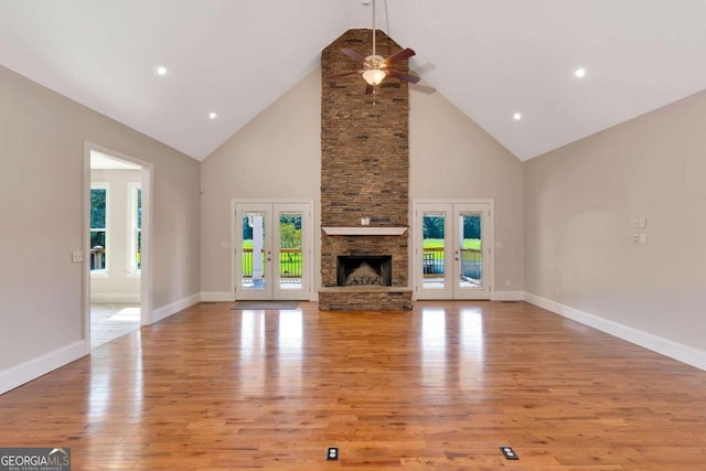 unfurnished living room with a fireplace, ceiling fan, light wood-type flooring, high vaulted ceiling, and french doors