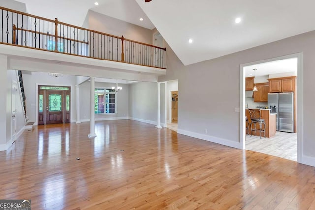 unfurnished living room featuring ornate columns, high vaulted ceiling, an inviting chandelier, and light wood-type flooring