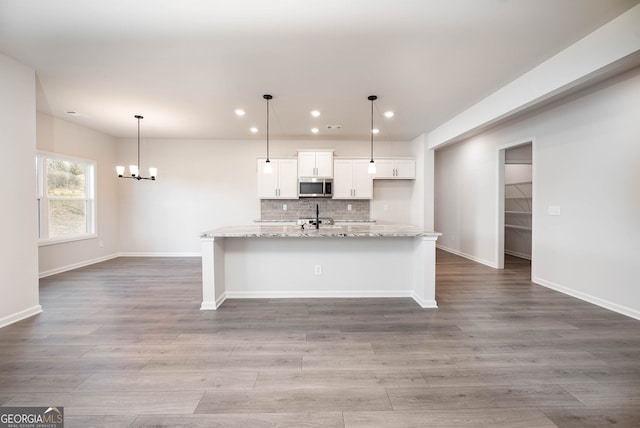 kitchen with white cabinetry, light stone counters, backsplash, decorative light fixtures, and a kitchen island with sink