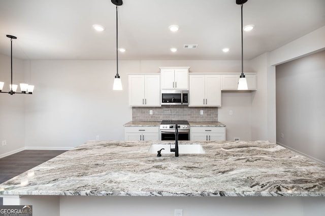 kitchen with decorative backsplash, appliances with stainless steel finishes, a large island with sink, decorative light fixtures, and white cabinets