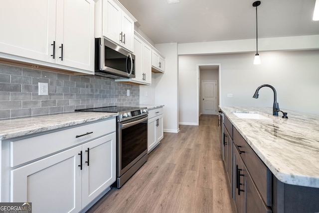 kitchen with white cabinets, sink, hanging light fixtures, light wood-type flooring, and stainless steel appliances