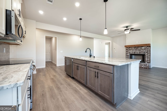 kitchen with sink, stainless steel appliances, hanging light fixtures, wood-type flooring, and a center island with sink