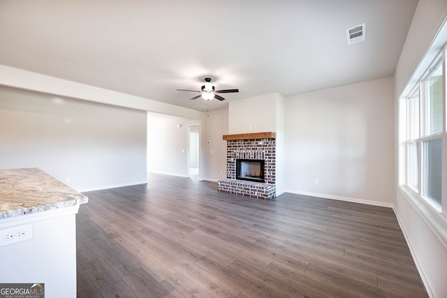 unfurnished living room featuring a fireplace, ceiling fan, plenty of natural light, and dark hardwood / wood-style floors