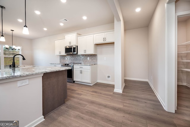 kitchen featuring hardwood / wood-style flooring, appliances with stainless steel finishes, decorative light fixtures, light stone counters, and white cabinetry