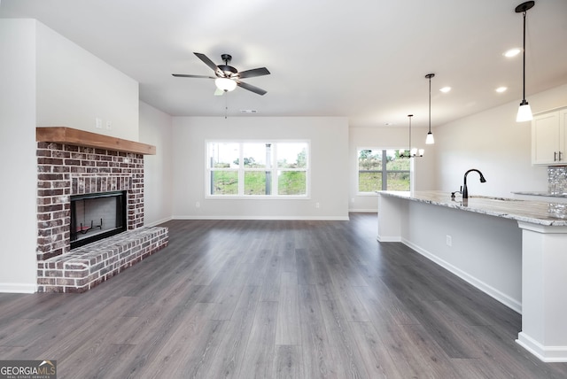 unfurnished living room with sink, ceiling fan with notable chandelier, dark hardwood / wood-style flooring, and a fireplace