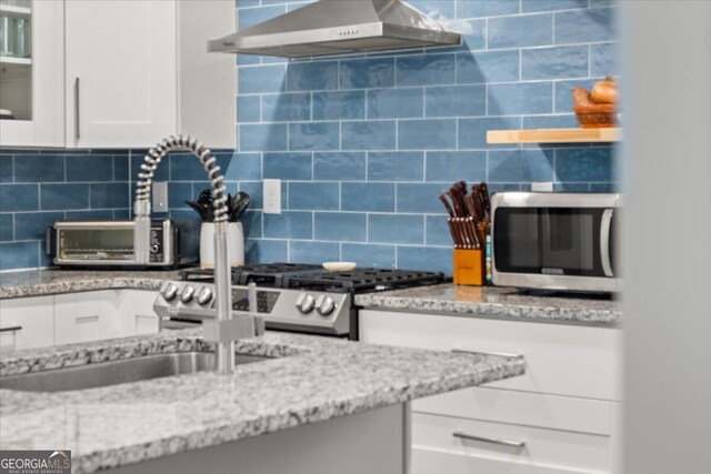 interior space featuring range, white cabinetry, backsplash, light stone counters, and wall chimney exhaust hood