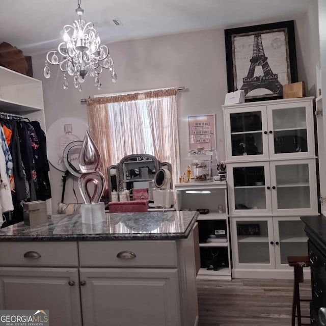 kitchen featuring dark hardwood / wood-style floors, an inviting chandelier, hanging light fixtures, dark stone counters, and white cabinets