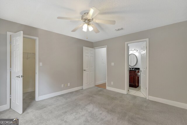 unfurnished bedroom with light colored carpet, ceiling fan, a walk in closet, and connected bathroom