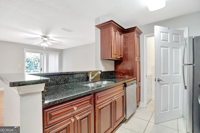 kitchen with a textured ceiling, appliances with stainless steel finishes, sink, ceiling fan, and dark stone counters