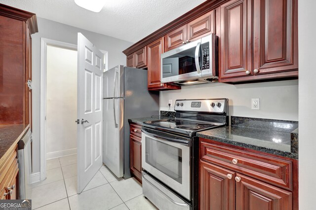 kitchen with light tile patterned floors, a textured ceiling, stainless steel appliances, and dark stone counters