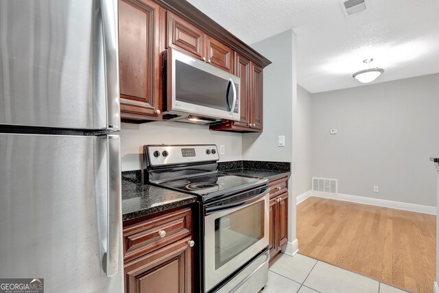 kitchen with light wood-type flooring, stainless steel appliances, dark stone counters, and a textured ceiling