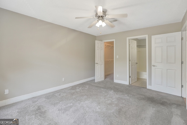 unfurnished bedroom featuring ensuite bathroom, light carpet, a walk in closet, a closet, and ceiling fan