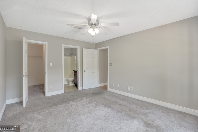 unfurnished bedroom with ceiling fan, light colored carpet, a spacious closet, and ensuite bath