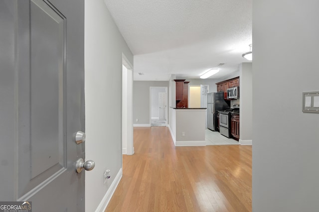 hall with light wood-type flooring and a textured ceiling