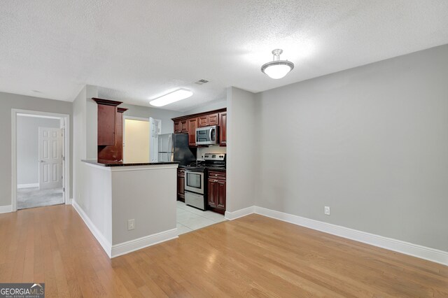 kitchen with appliances with stainless steel finishes, a textured ceiling, and light hardwood / wood-style flooring