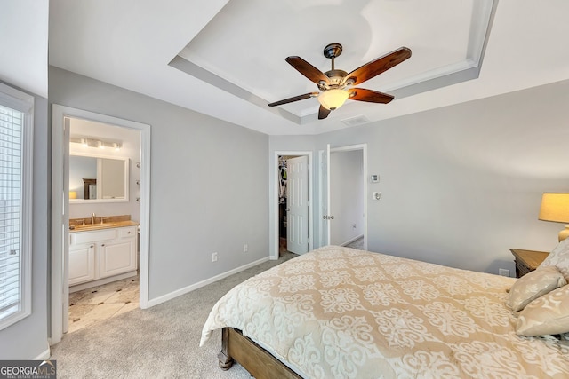 bedroom with ensuite bathroom, ceiling fan, light carpet, and a tray ceiling