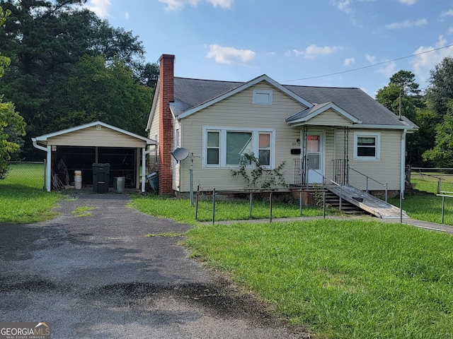 bungalow-style house featuring a chimney, aphalt driveway, fence, a front yard, and a detached carport