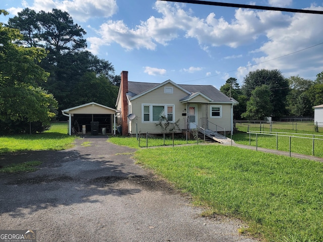 bungalow-style home featuring aphalt driveway, fence, a carport, a chimney, and a front yard