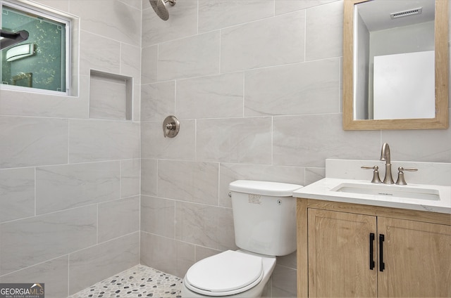 bathroom with vanity, tile walls, toilet, and tiled shower