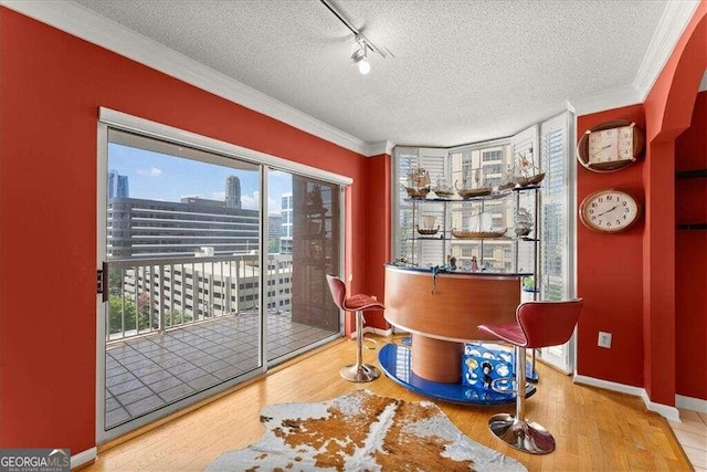 interior space with a textured ceiling, baseboards, wood finished floors, and crown molding