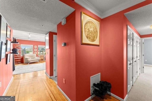 hallway featuring light wood finished floors, baseboards, visible vents, and a textured ceiling