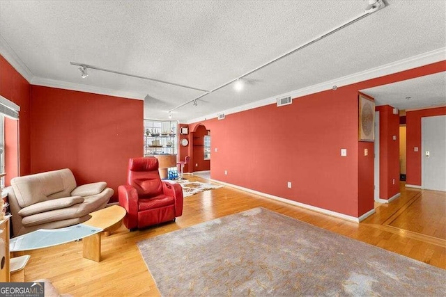 sitting room with arched walkways, a textured ceiling, wood finished floors, visible vents, and ornamental molding