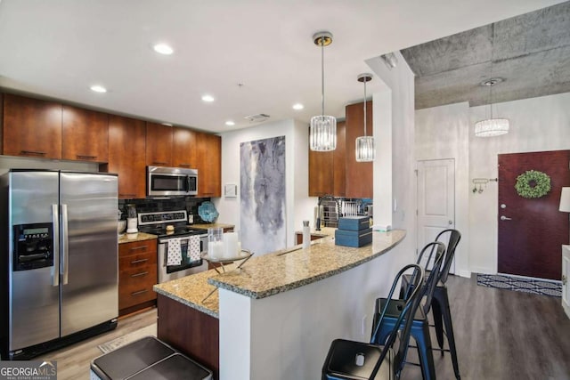 kitchen with light stone countertops, light wood-type flooring, decorative light fixtures, kitchen peninsula, and stainless steel appliances