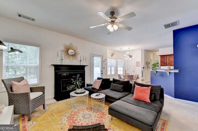 carpeted living room with ceiling fan with notable chandelier and a fireplace