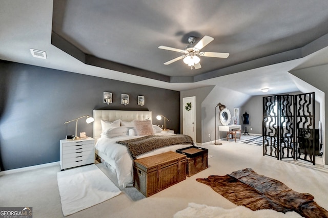 carpeted bedroom with a raised ceiling and ceiling fan