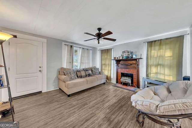 living room featuring ceiling fan, wood-type flooring, and a brick fireplace