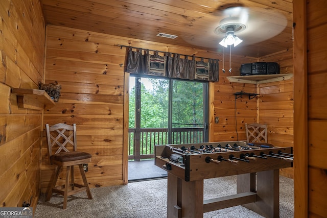 recreation room featuring wooden walls, wooden ceiling, ceiling fan, and carpet flooring