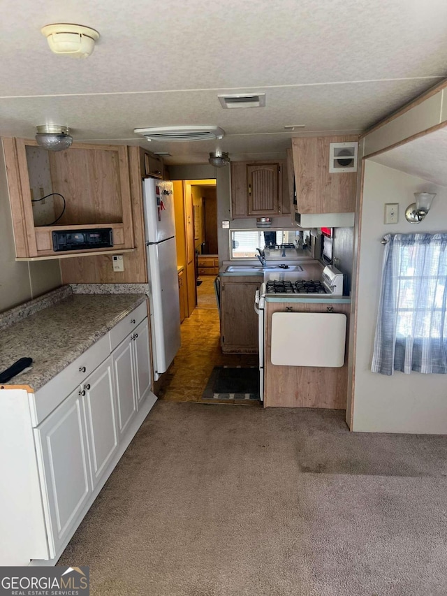 kitchen with range with gas cooktop, sink, refrigerator, white cabinetry, and light carpet