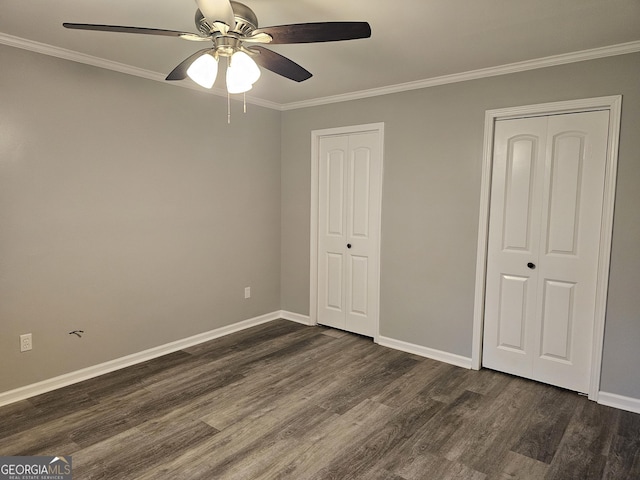 unfurnished bedroom with dark hardwood / wood-style flooring, two closets, ornamental molding, and ceiling fan