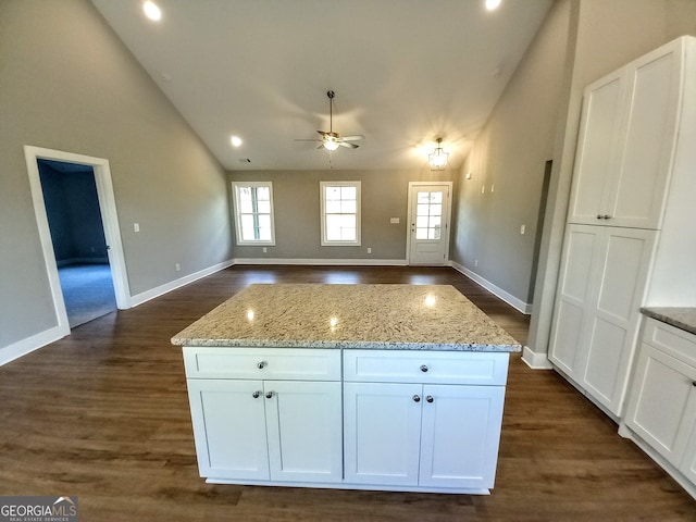 kitchen with light stone countertops, lofted ceiling, a kitchen island, and white cabinetry