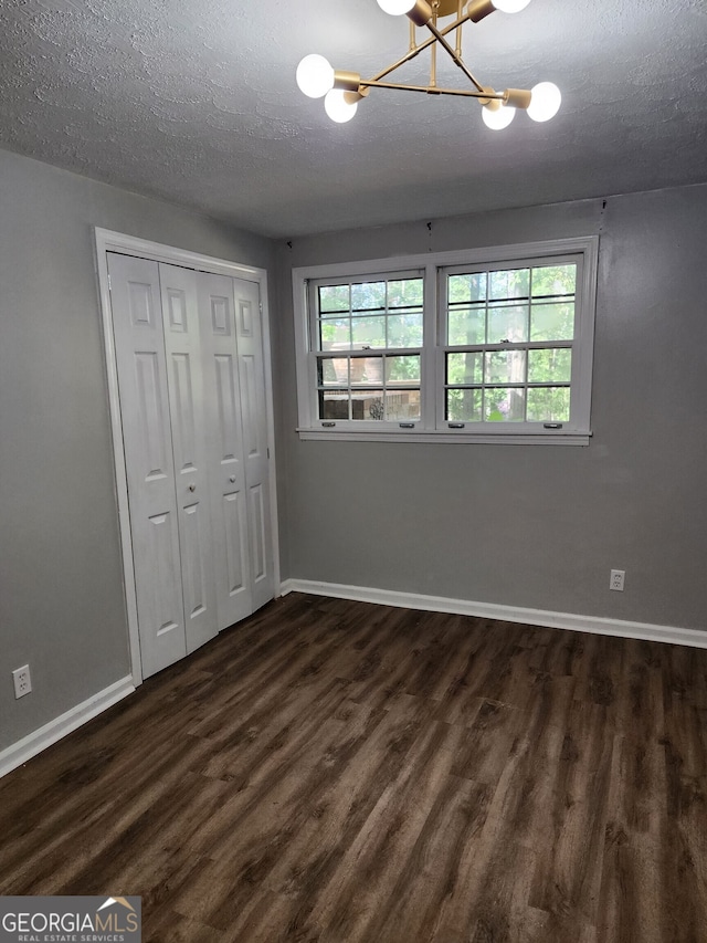 unfurnished bedroom with a closet, dark hardwood / wood-style floors, a textured ceiling, and a notable chandelier