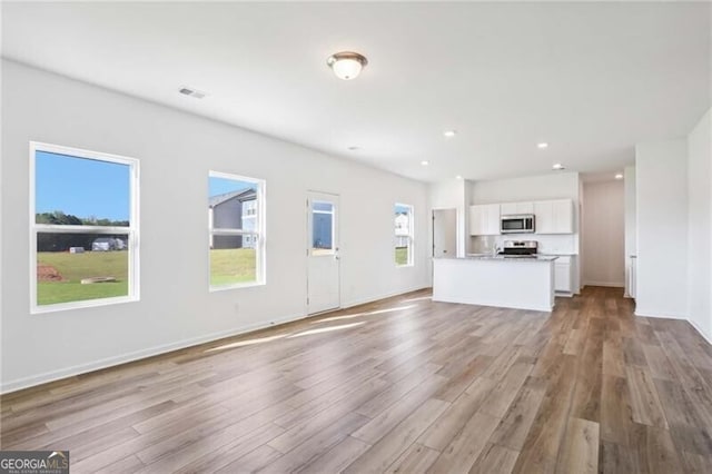 kitchen with sink, white cabinetry, stainless steel appliances, a center island with sink, and light stone countertops