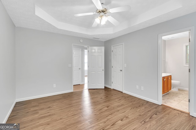 unfurnished bedroom featuring a tray ceiling, ensuite bathroom, a textured ceiling, and light wood-type flooring