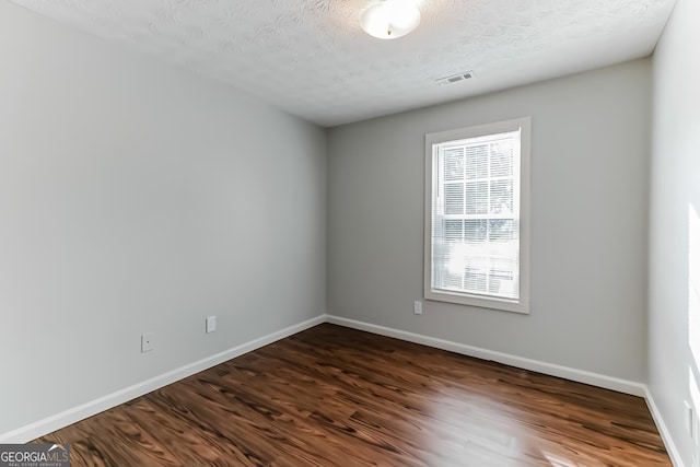 empty room with dark wood-type flooring and a textured ceiling