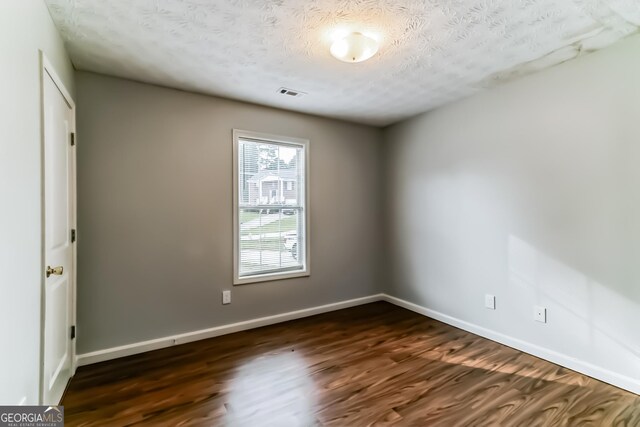 empty room with dark wood-type flooring and a textured ceiling