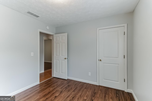 unfurnished bedroom featuring a textured ceiling and dark hardwood / wood-style flooring