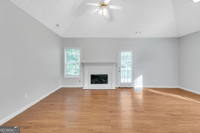 unfurnished living room featuring a tile fireplace, vaulted ceiling, ceiling fan, and light hardwood / wood-style floors