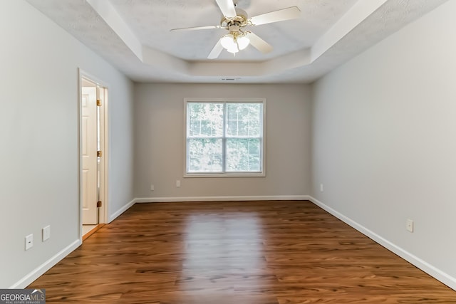 unfurnished room with a raised ceiling, dark wood-type flooring, and ceiling fan