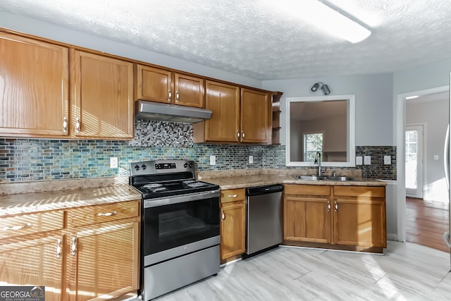 kitchen featuring sink, a textured ceiling, stainless steel appliances, light stone countertops, and backsplash