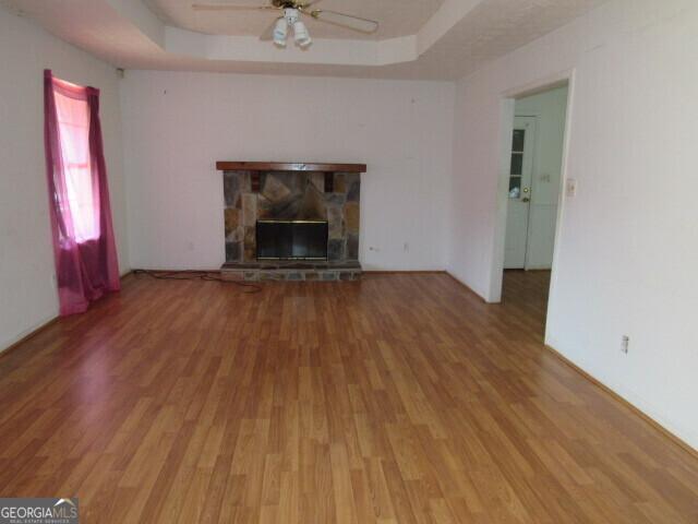 unfurnished living room featuring hardwood / wood-style floors, a raised ceiling, a stone fireplace, and ceiling fan