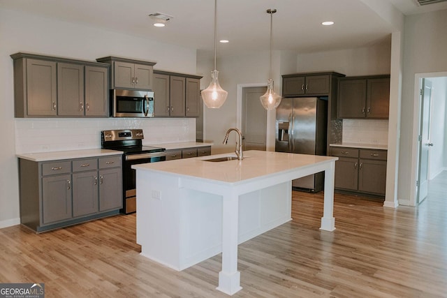 kitchen featuring sink, a kitchen island with sink, stainless steel appliances, light hardwood / wood-style floors, and decorative light fixtures