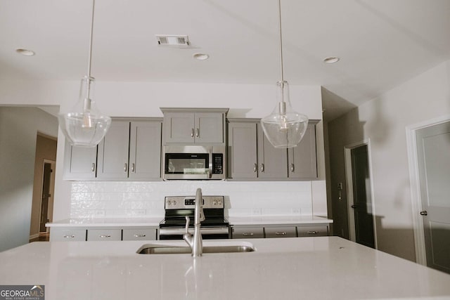 kitchen with gray cabinetry, decorative light fixtures, tasteful backsplash, and stainless steel appliances